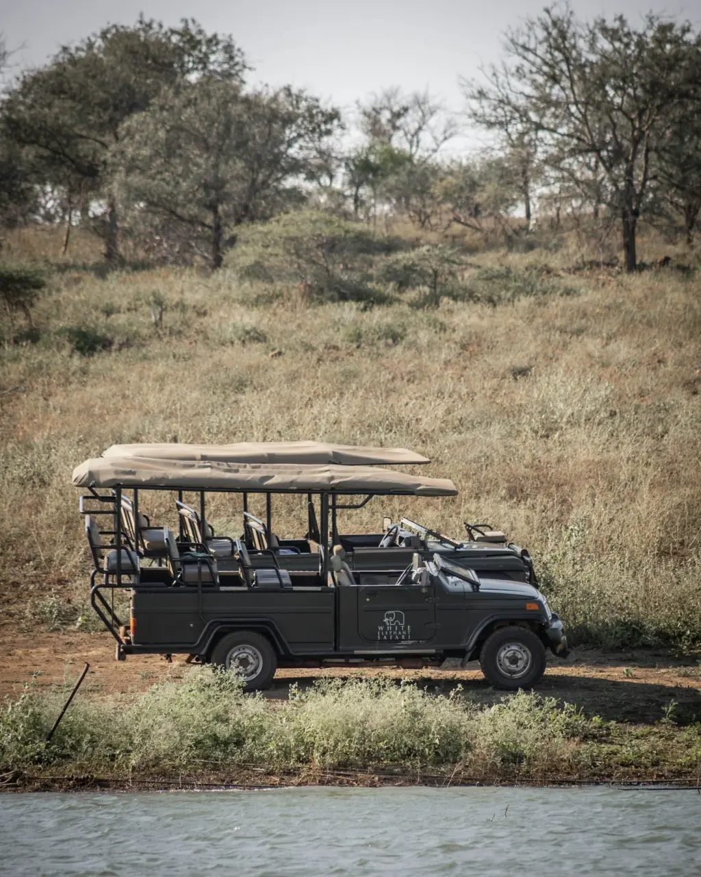 An open-sided safari vehicle parked in dry grassland. Illustrative photograph.